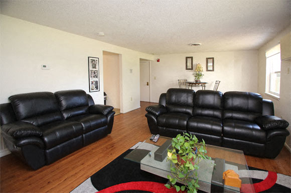 A black leather couch in a living room with a glass coffee table in front of it.