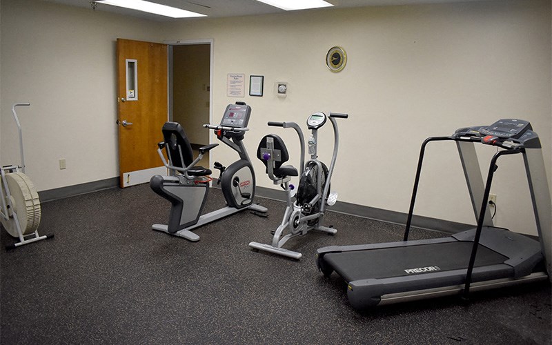 A gym room with a treadmill, elliptical trainer, and a stationary bike.