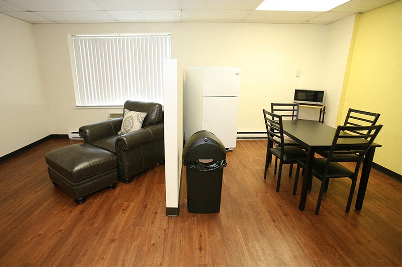 A room with a brown leather chair, a black trash can, and a white refrigerator.