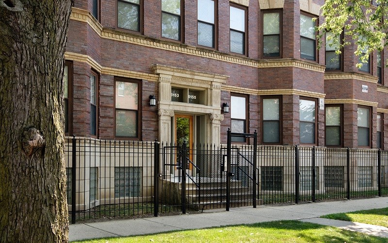 A brown building with a black fence and a tree in front.