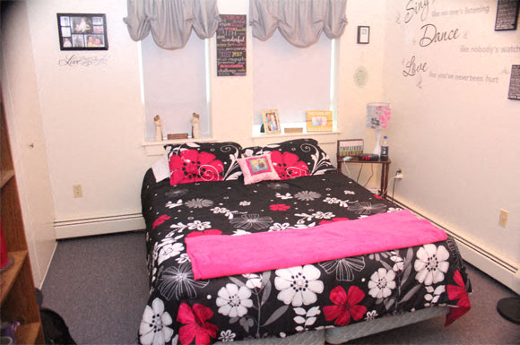 A bedroom with a bed covered in a black and pink floral comforter.