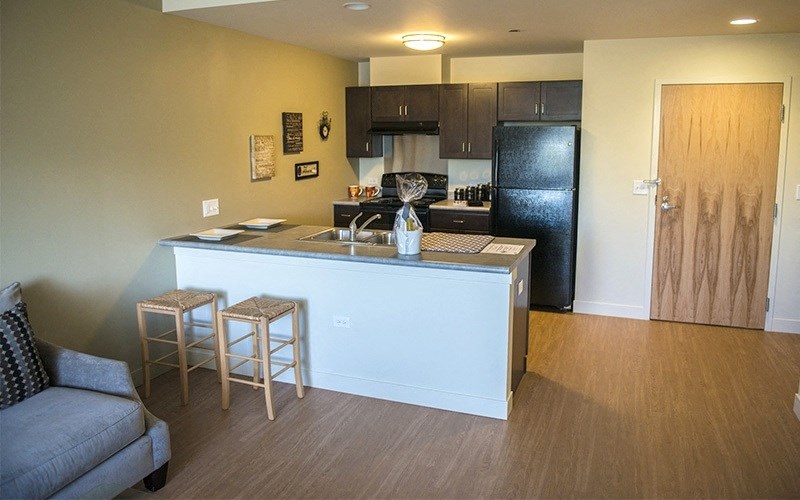 A kitchen with a black fridge and wooden floors.