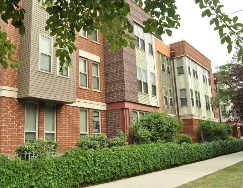 A row of red brick apartment buildings with green bushes in front.