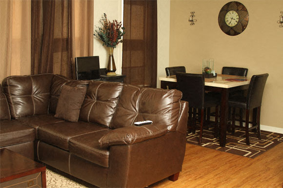 A brown leather couch in a living room with a dining table and chairs in the background.