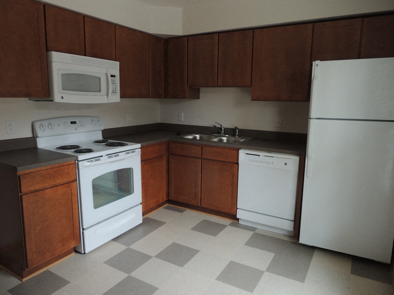 an empty kitchen with white appliances and wooden cabinets
