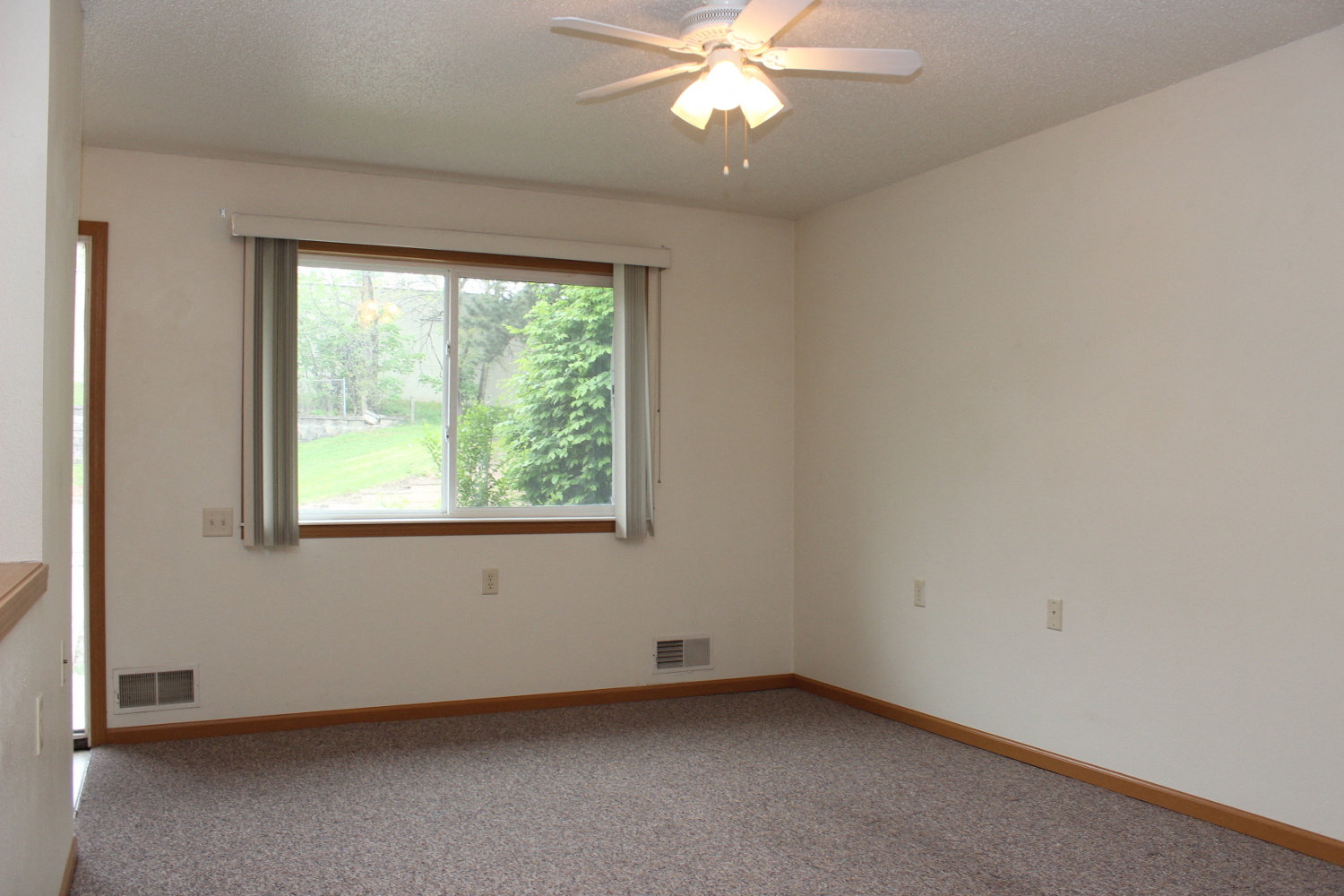 an empty living room with a window and a ceiling fan
