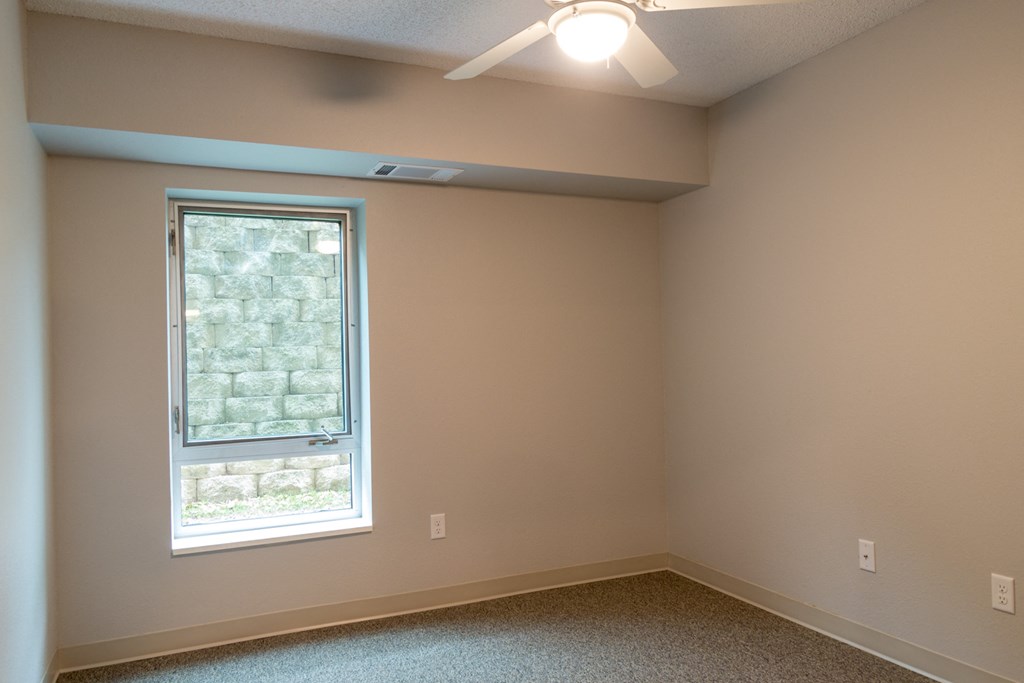 an empty bedroom with a window and a ceiling fan