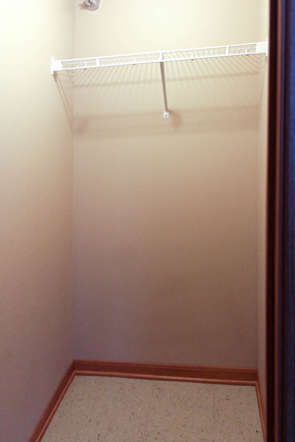 a walk in shower in a white room with a shelf