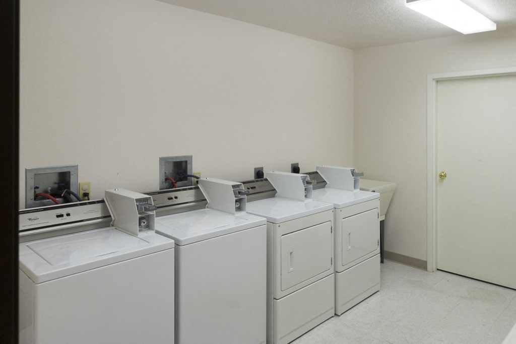 a row of washers and dryers in a laundry room with four washing machines