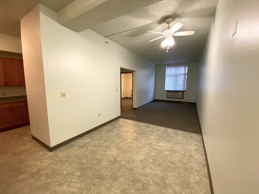 an empty living room with a ceiling fan and white walls