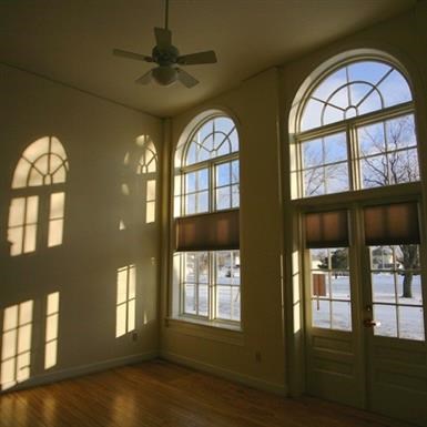 an empty living room with large windows and a ceiling fan