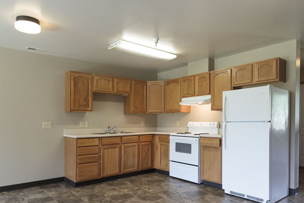 an empty kitchen with white appliances and wooden cabinets