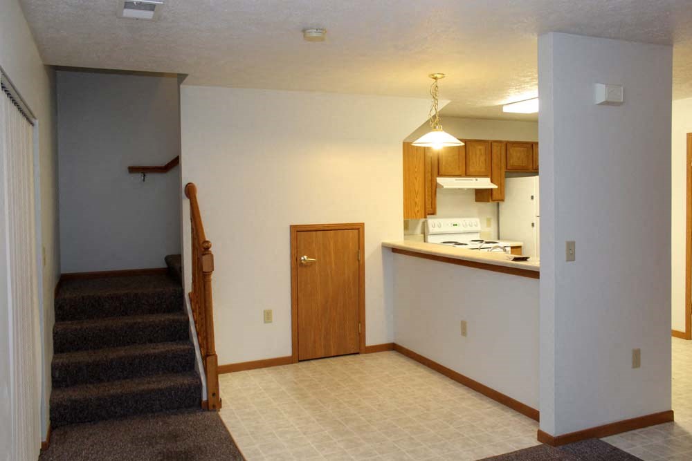 an empty living room with a kitchen and stairs