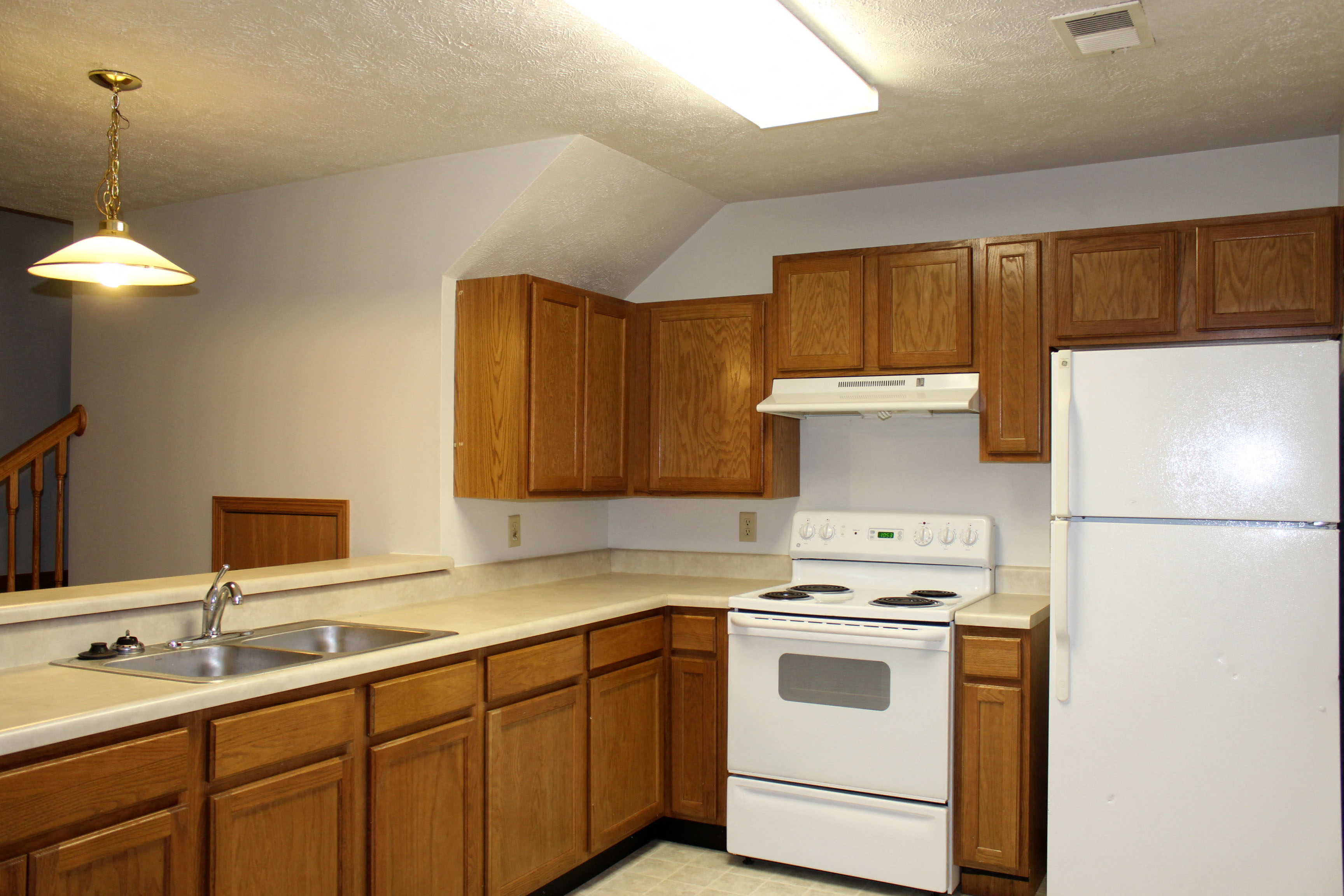 an empty kitchen with white appliances and wooden cabinets