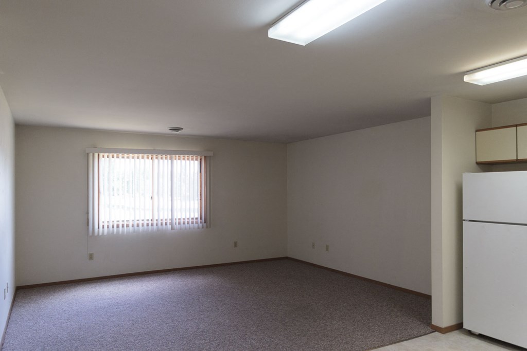 an empty living room with a window and a refrigerator
