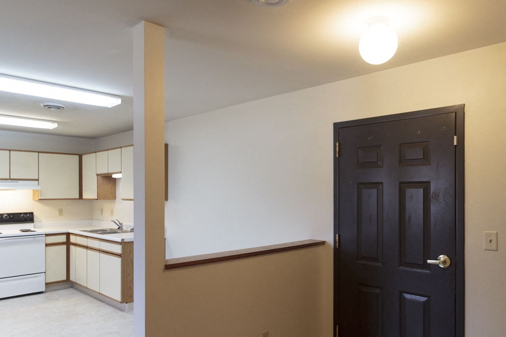 an empty room with a black door and a kitchen