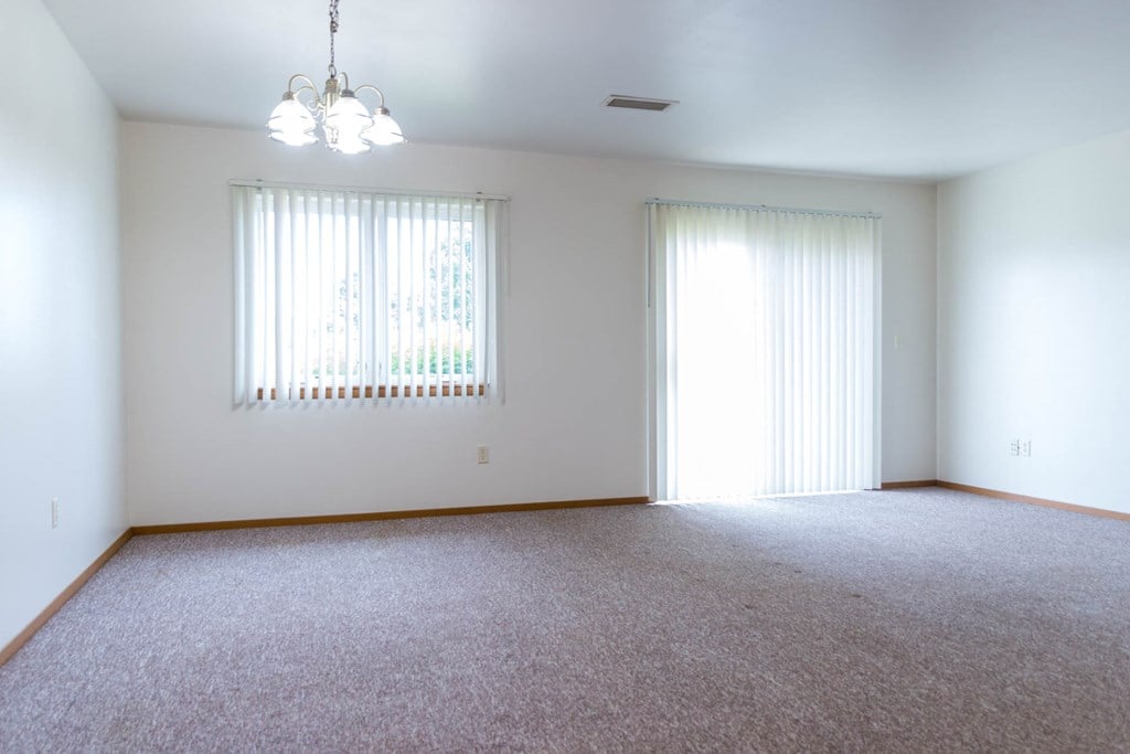 an empty living room with two windows and carpet