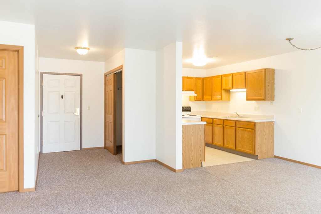 an empty kitchen and living room with wood cabinets and white flooring