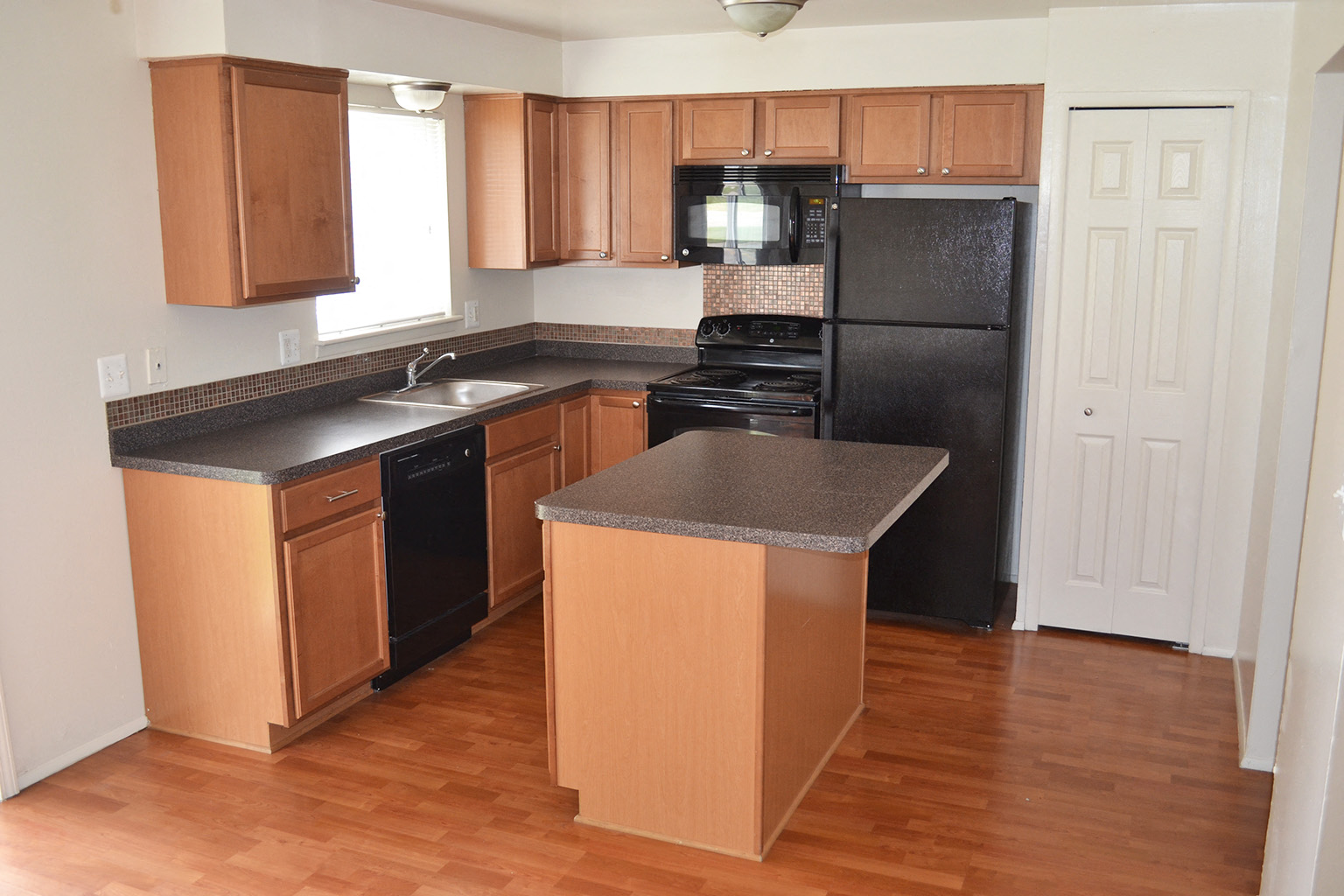 an empty kitchen with wooden cabinets and a black refrigerator