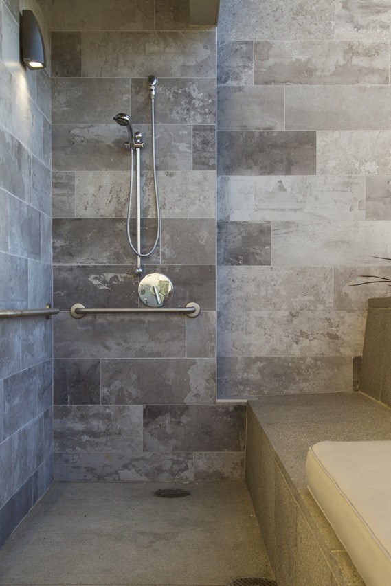a gray tiled bathroom with a shower and a hand rail