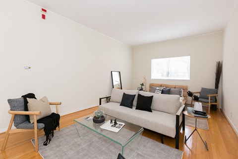 A living room with a grey couch, a glass coffee table, and a wooden chair.