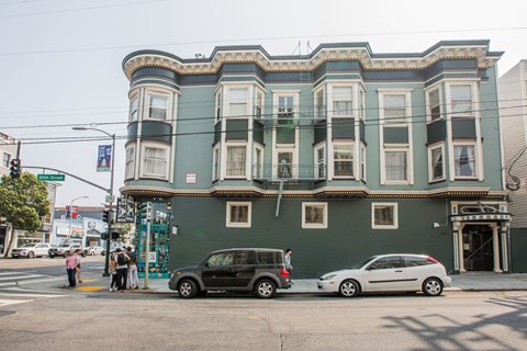 A green building with a black car and white car parked in front.