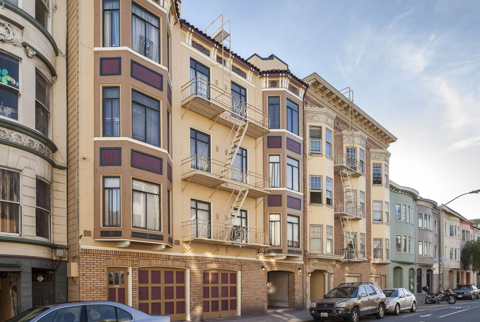 A row of apartment buildings with cars parked in front.