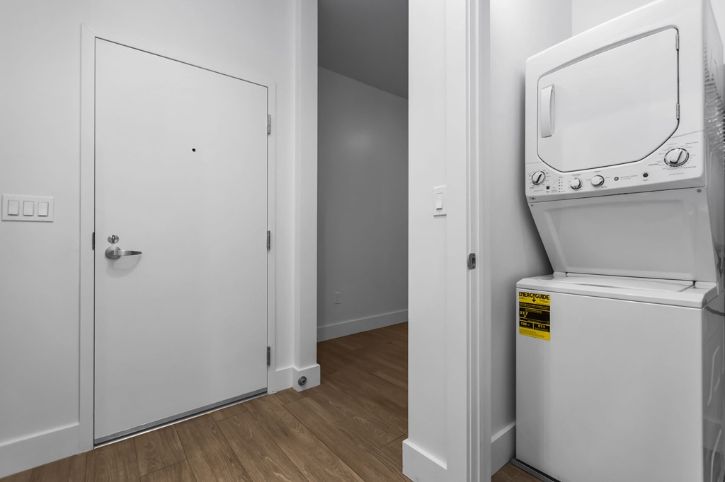A white door with a handle is open to a room with a white fridge.