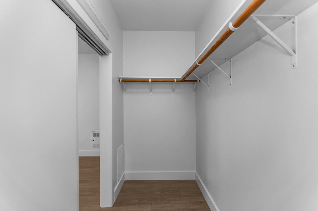 A white room with a wooden floor and a white wall with a white door and a white shelf.