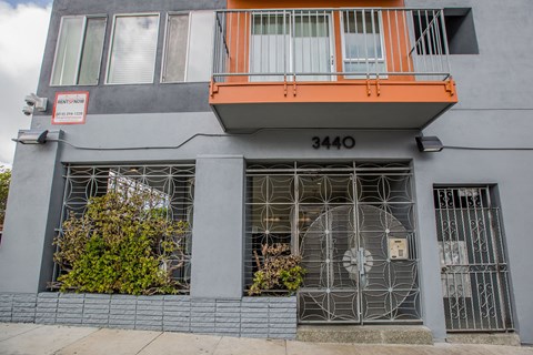 A grey building with a red sign on the left and a balcony on the right.