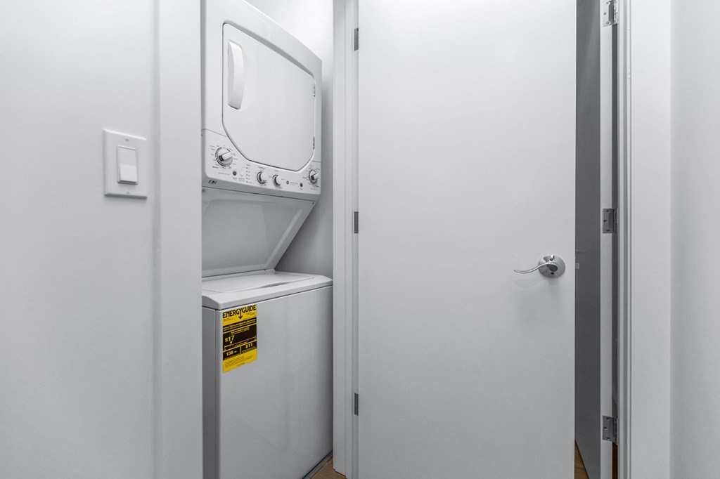 A small white washing machine is in a narrow space between a wall and a door.