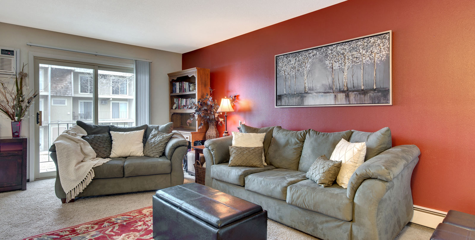 A living room with a grey couch, a red rug, and a painting on the wall.