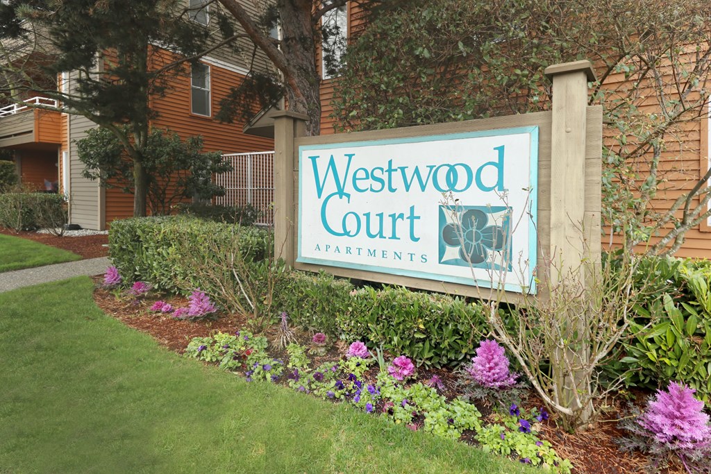 A sign for Westwood Court Apartments is surrounded by flowers and greenery.