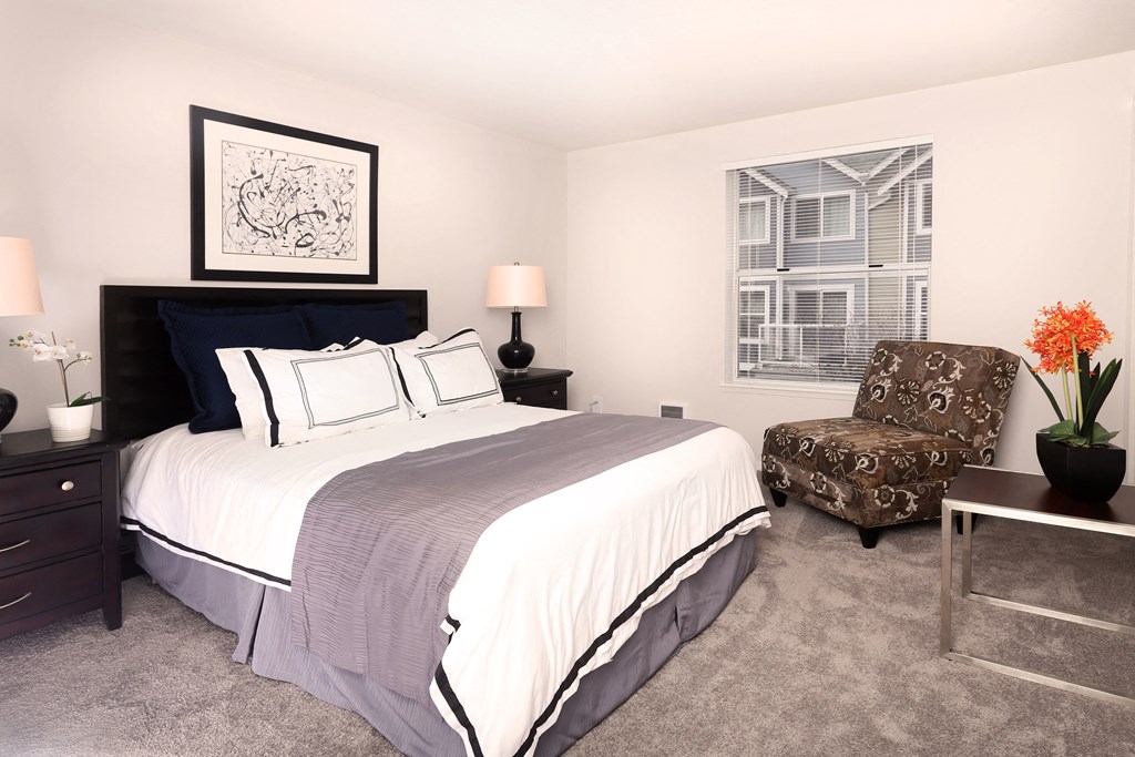 A bedroom with a bed, chair, and two lamps.