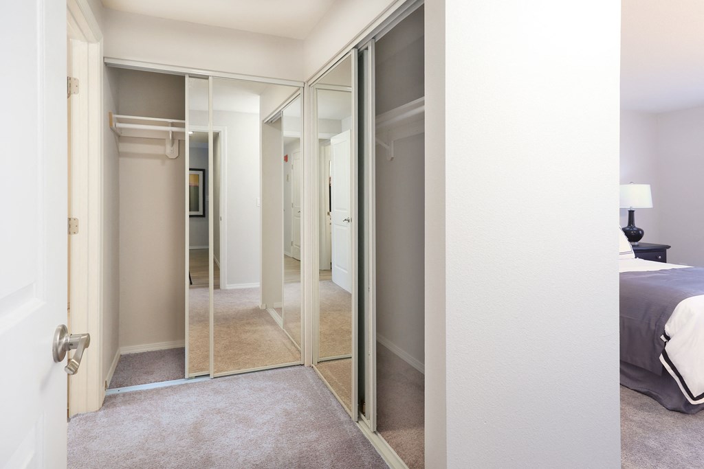 A bedroom with a large mirrored wardrobe and a bed with a white comforter.