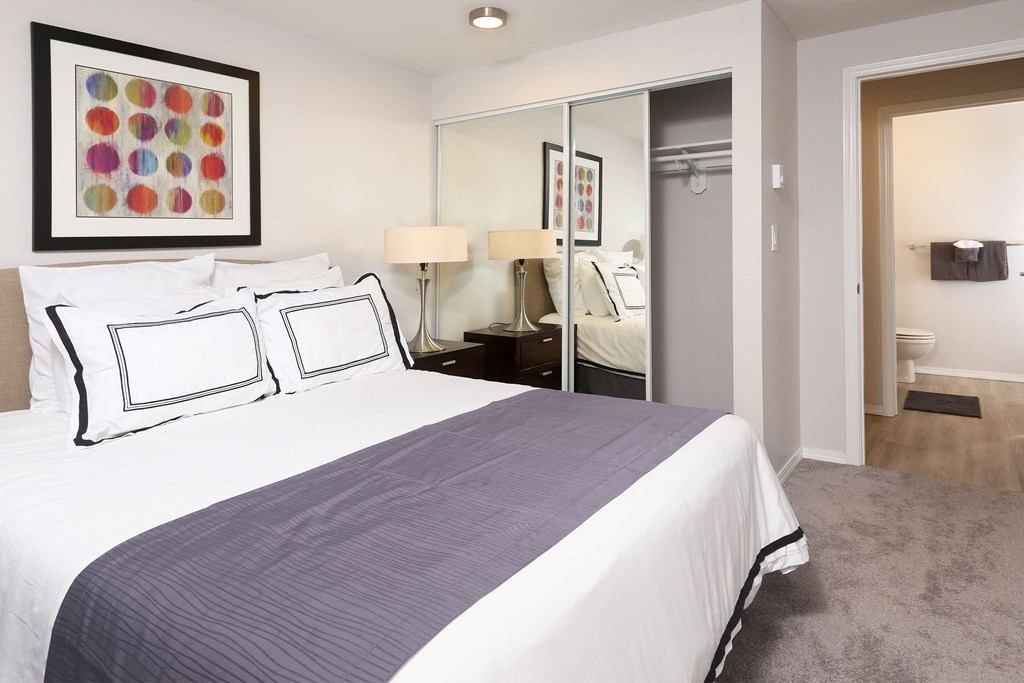 A bedroom with a large bed and a mirrored closet door.