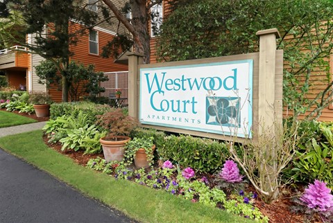 A sign for Westwood Court Apartments is surrounded by flowers and plants.