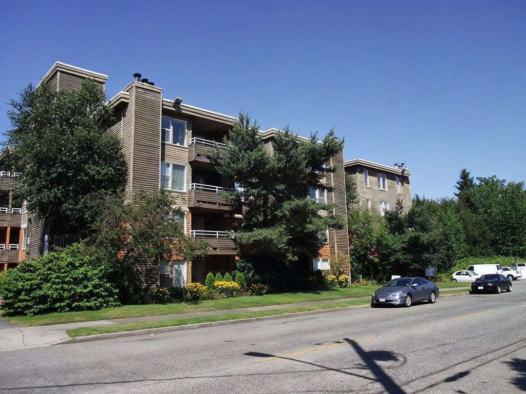 A car is driving down a street past apartment buildings.