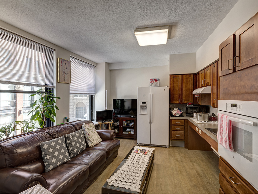 a living room with a leather couch and a kitchen with a refrigerator