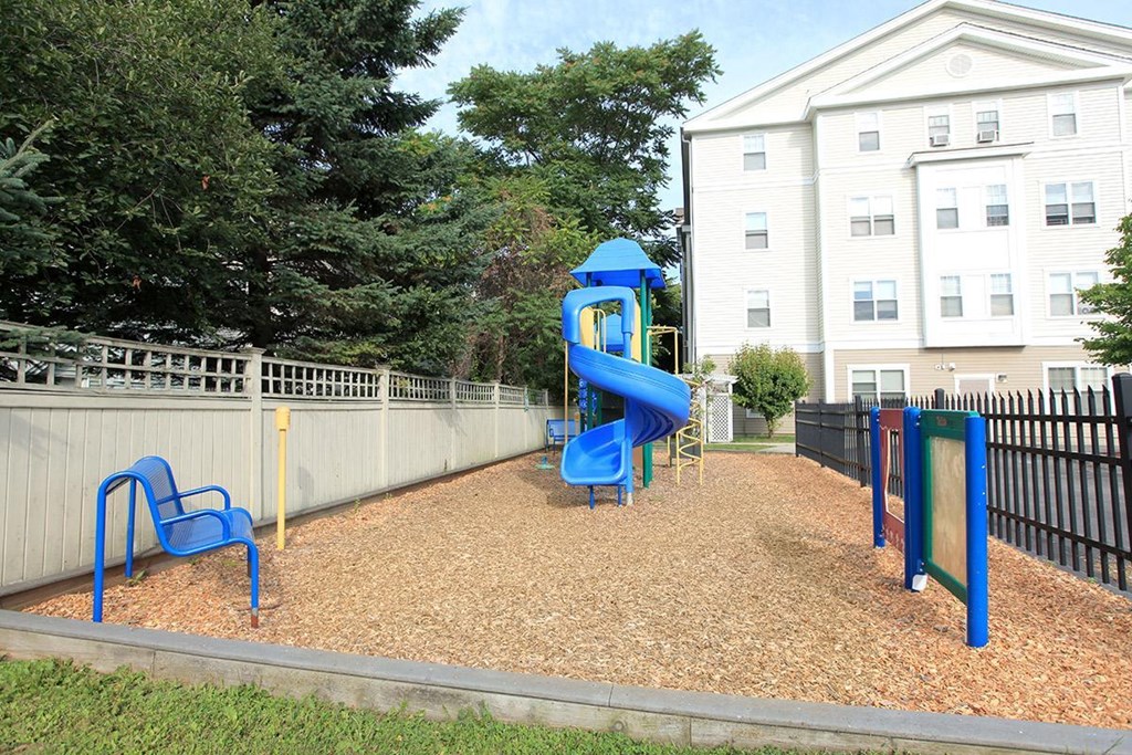 a playground with a slide and chairs in front of a fence