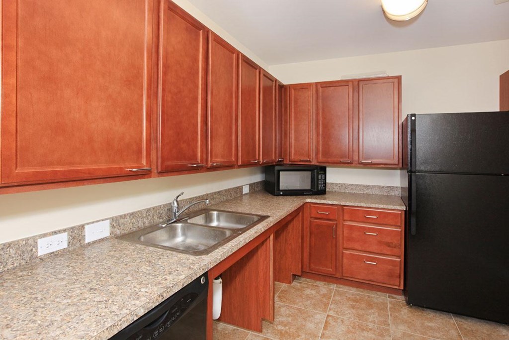 a kitchen with wood cabinets and a sink and a black refrigerator