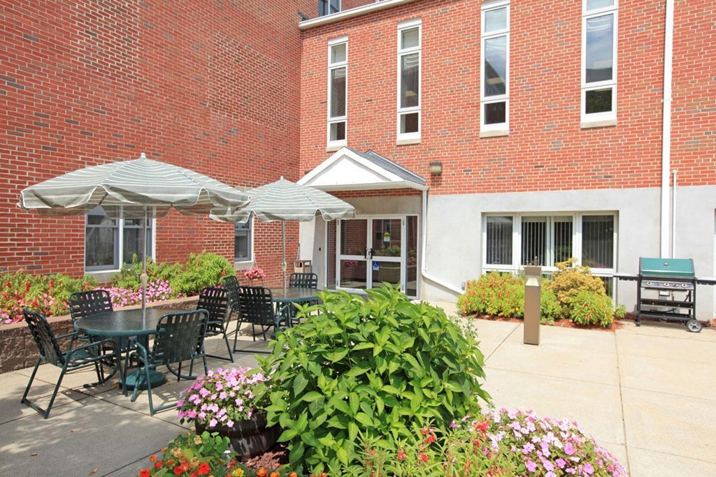 a patio with tables and umbrellas in front of a brick building