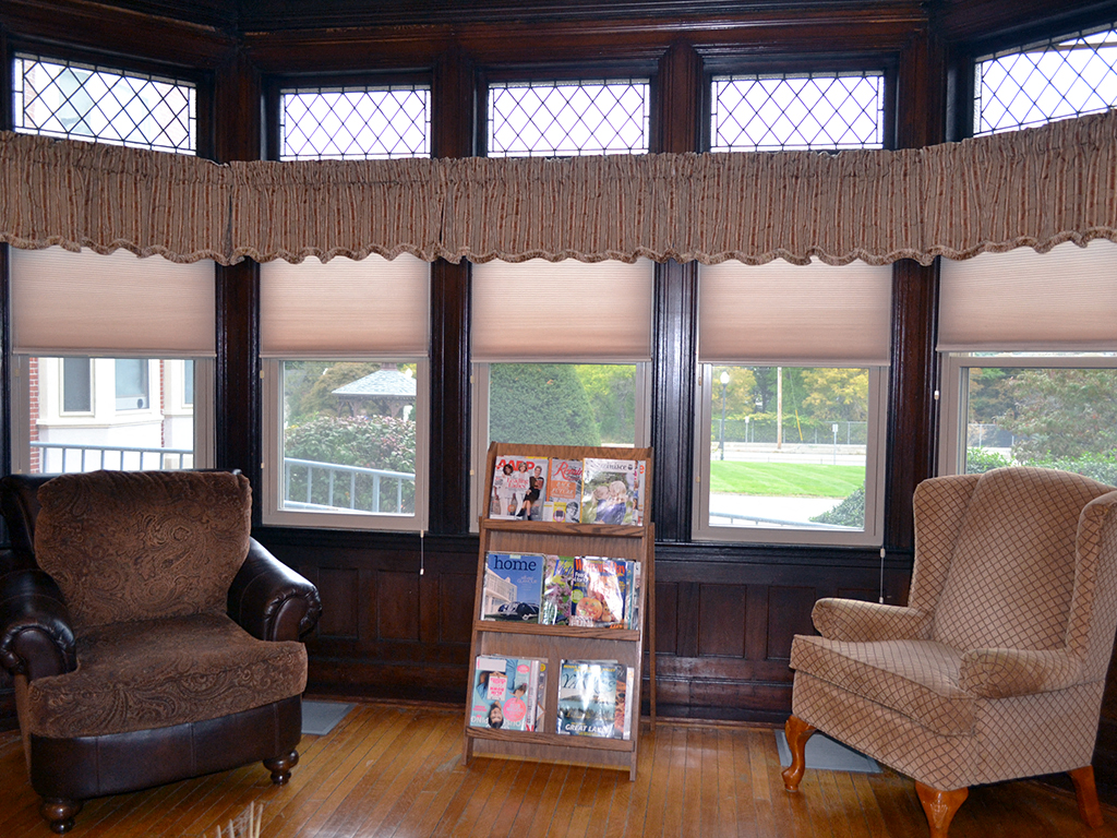 a living room with chairs and windows with a book shelf