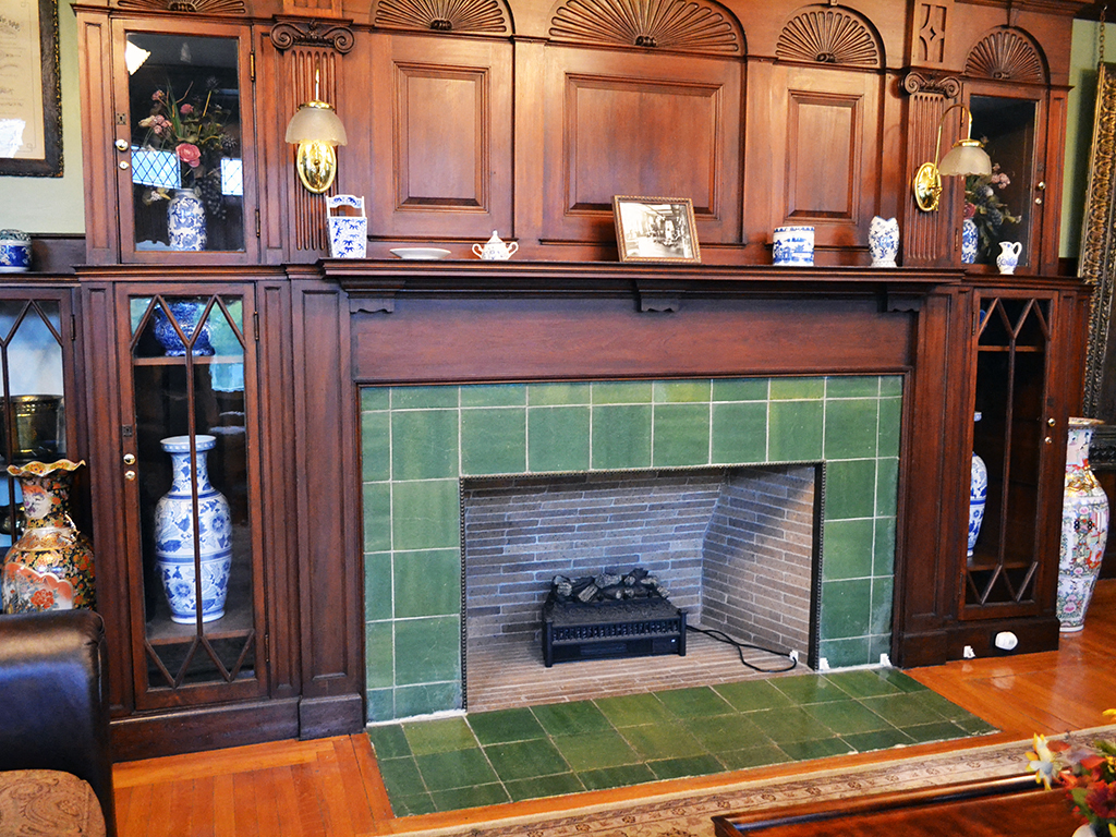 the fireplace in the living room has green tile and a wood mantle