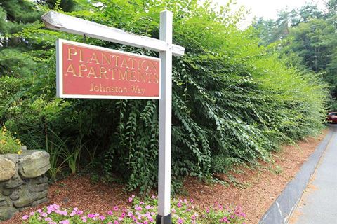 a sign for plantation apartments in front of a garden