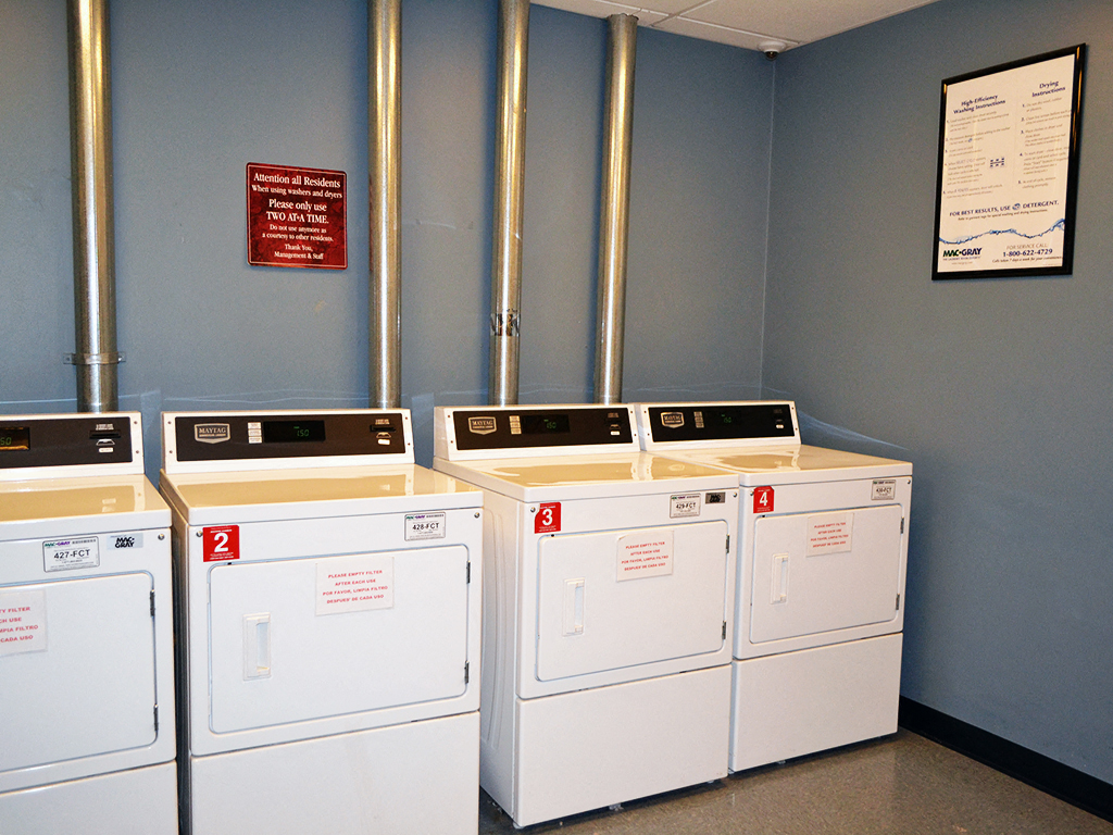 four washing machines lined up against a wall in a laundry room