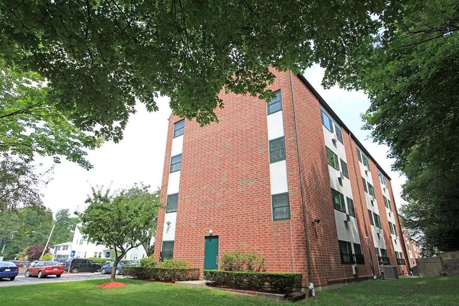 a brick building with a green lawn and trees