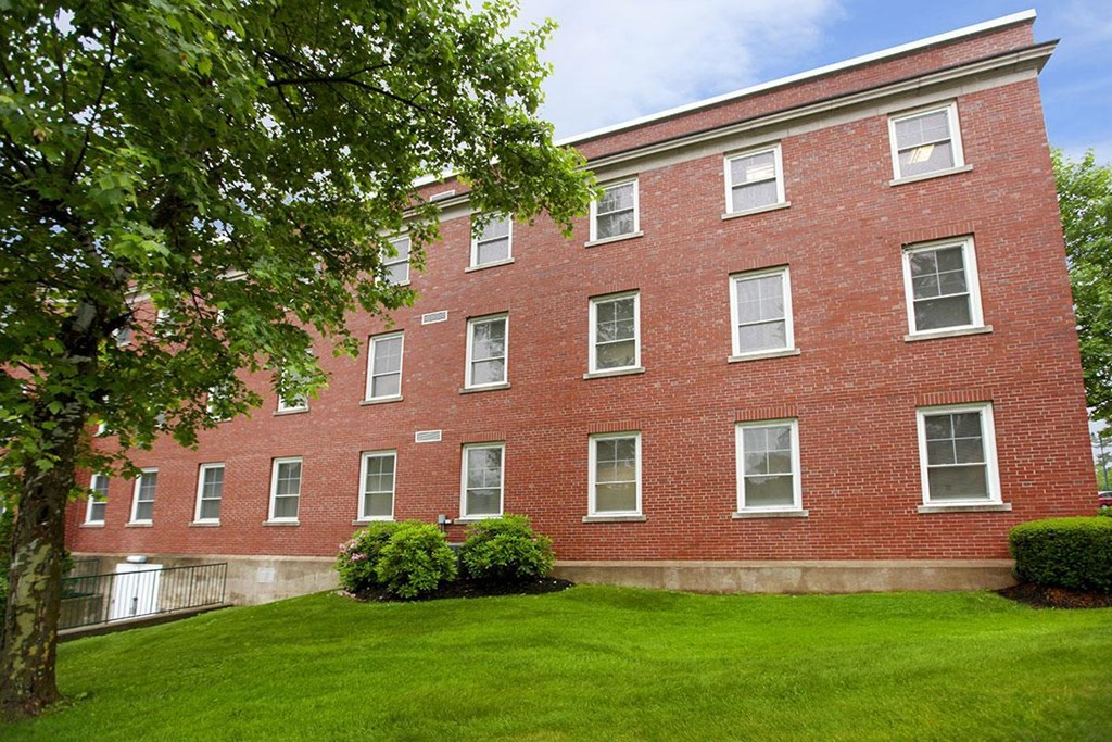 a red brick building with green grass and a tree