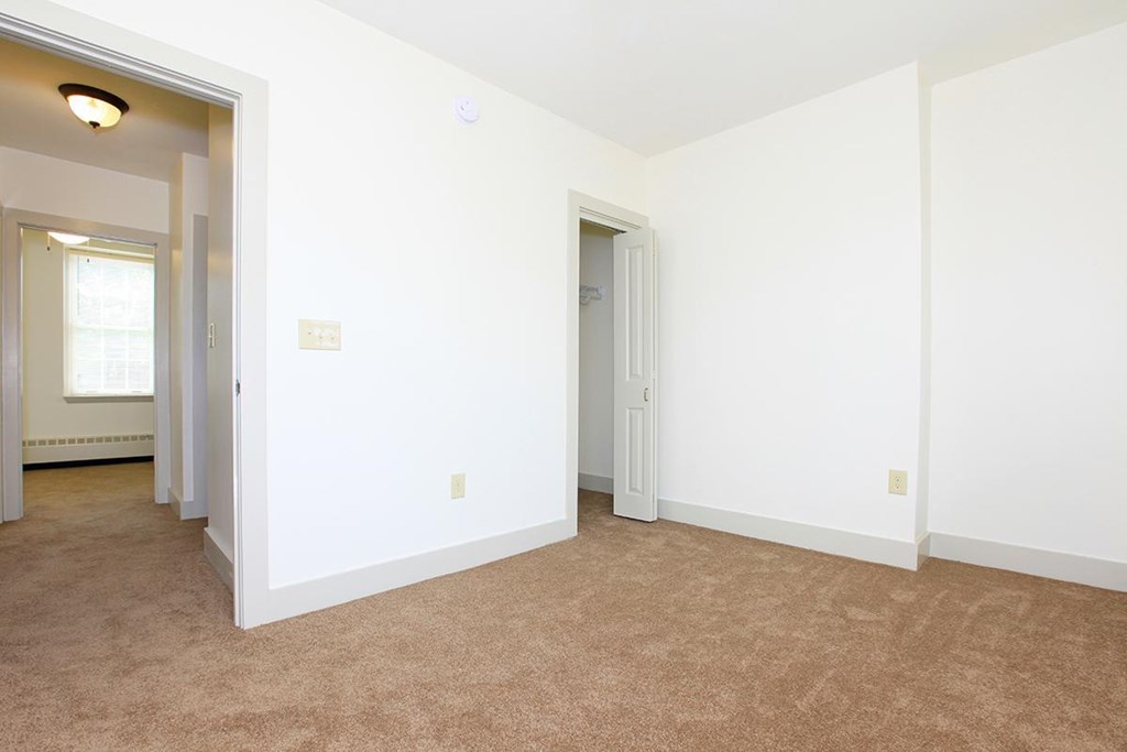 a bedroom with white walls and carpet and a door to a closet