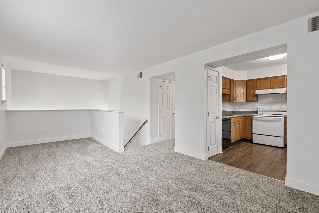 a living and kitchen area with white walls and a carpeted floor